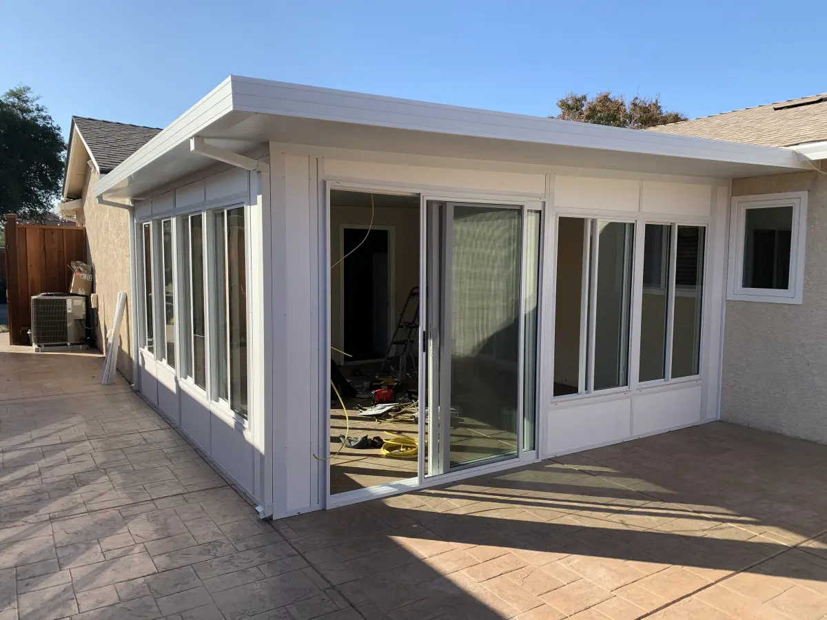 White insulated sunroom addition with sliding glass doors on a stamped-concrete patio