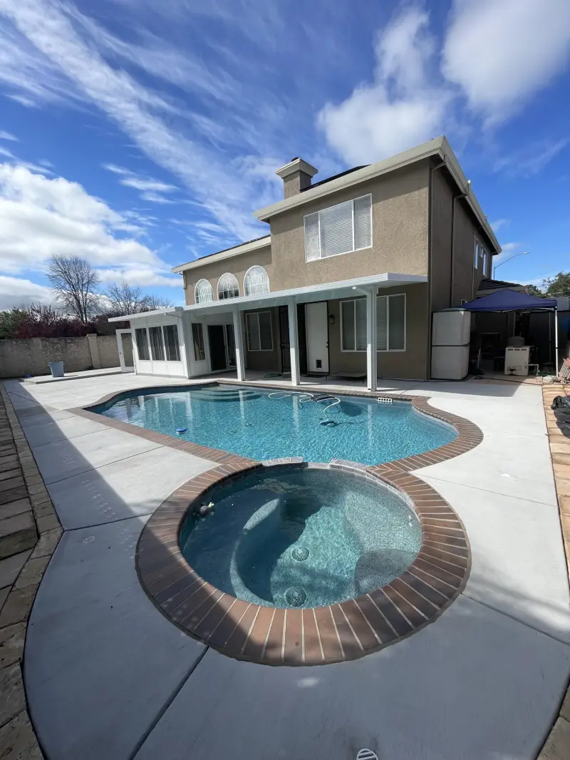 Two-story home with a white patio cover and sunroom overlooking a pool and spa
