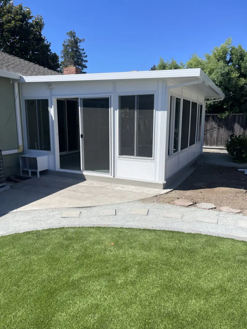 White sunroom addition with sliding door and wraparound windows beside a lawn