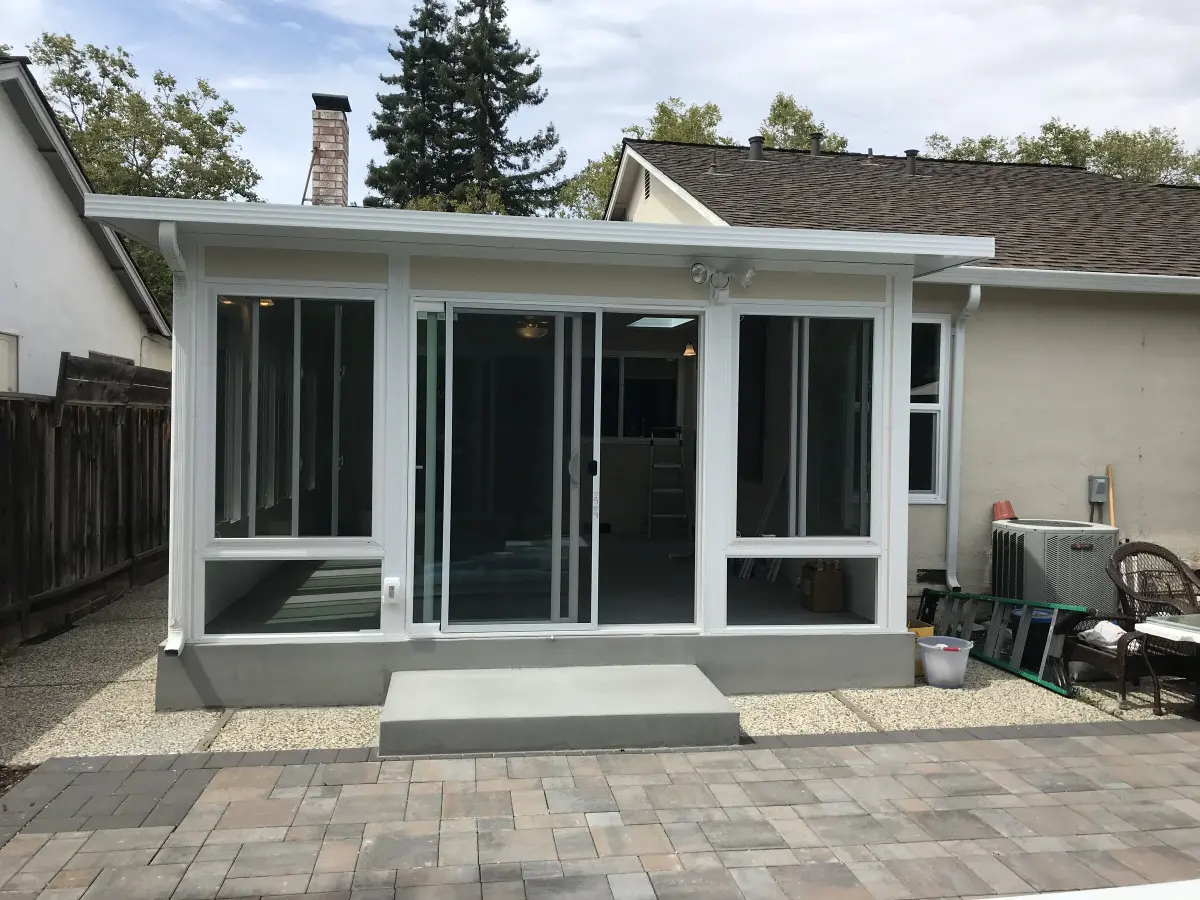 White sunroom addition with sliding glass doors and a concrete step onto a paver patio