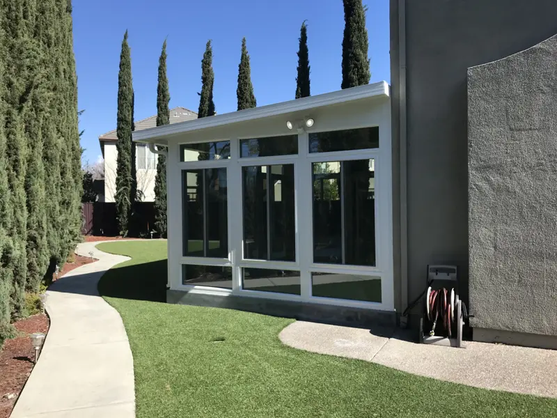 White glass sunroom beside a curving garden path lined with tall cypress trees