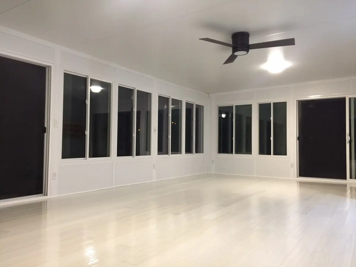 Bright, finished sunroom interior with white walls, rows of windows, sliding doors, and a ceiling fan